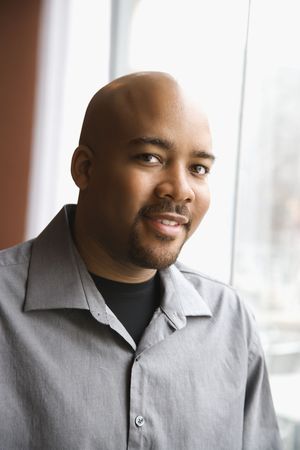 Head and shoulders portrait of an attractive African-American man smiling near a window. Vertical shot.の写真素材
