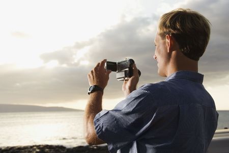 Smiling Caucasian man photographing a scenic sunset at a beach. Horizontal format.の写真素材