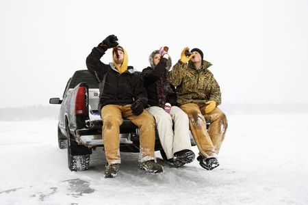 Two young men and a young woman drinking beer while sitting on the tailgate of a truck in a winter environment. Horizontal shot.の写真素材