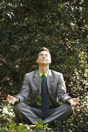 Young businessman sits in a lotus position meditating in the woods with closed eyes and a smile.の写真素材