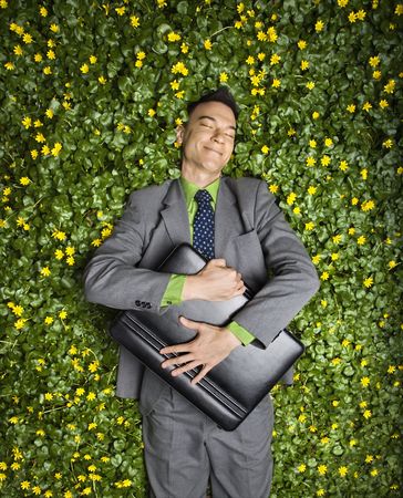 Young businessman with briefcase relaxing in a flower patch smiling with contentment.の写真素材