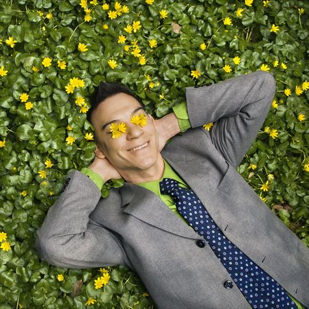 Young smiling businessman relaxing in a flower patch with flowers over his eyes.の写真素材