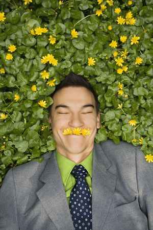 Young smiling businessman relaxing in a flower patch wearing flowers over his mouth like a mustache.の写真素材