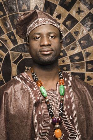 Portrait of an African American man wearing traditional African clothing, in front of a patterned wall and looking at the camera. Vertical format.の写真素材