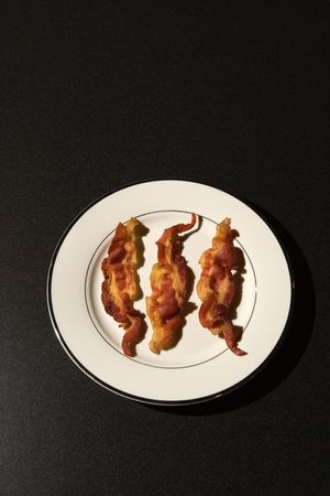Three strips of cooked bacon on a white plate. Vertical shot.の写真素材