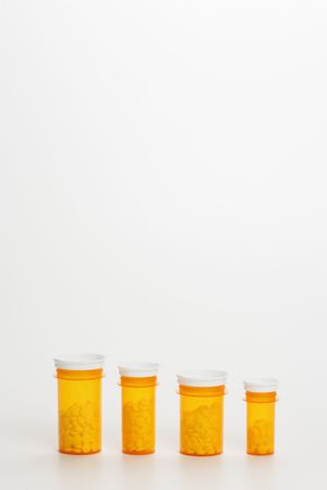Yellow medicine bottles with pills in diminishing sizes lined up in a row. Vertical shot. Isolated on white.の写真素材