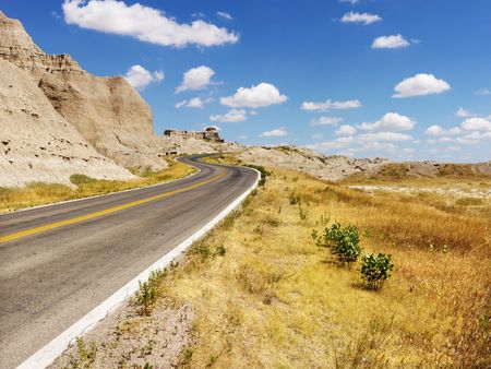 Rural road by rock formations and a field in Badlands National Park, South Dakota. Horizontal shot.の写真素材