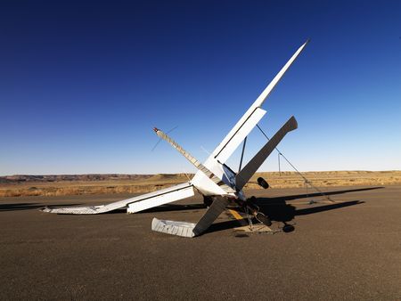 A small, crashed aircraft in a desert landscape. It is on its side with a broken wing and tail....