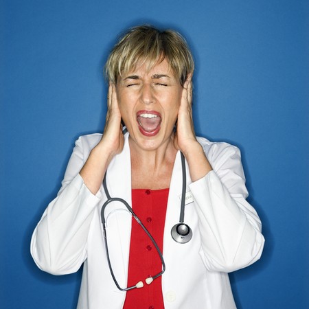 Caucasian female doctor holding hands to ears and screaming.の写真素材
