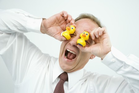 Portrait of middle aged  Caucasian businessman playing with rubber ducks making funny face.の写真素材