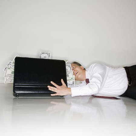 Caucasian middle aged businessman grabbing at briefcase overflowing with money.の写真素材