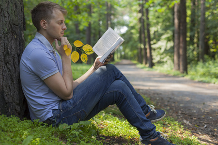 A young man is reading a book in a summer parkの写真素材