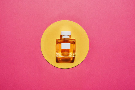 top view of bottle of perfume on yellow circle with copy space on pink backgroundの素材