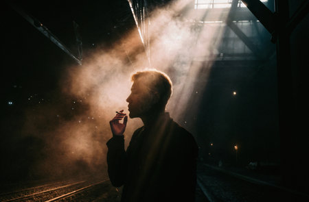 Side view portrait of a man smoking cigarette and looking away while standing at the railway stationの素材