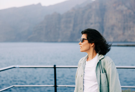 A woman stands facing the ocean on Tenerife, Canary Islands, gazing into the distance and...