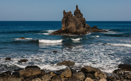 A dramatic coastal scene featuring a rugged rock formation surrounded by ocean waves and a rockyの写真素材