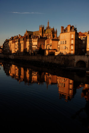 Golden hour cityscape with historic buildings reflected in calm river water.の写真素材