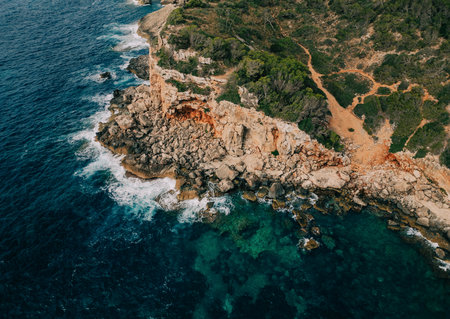 Rocky coastal cliff with green vegetation and turquoise waters crashing below.の写真素材