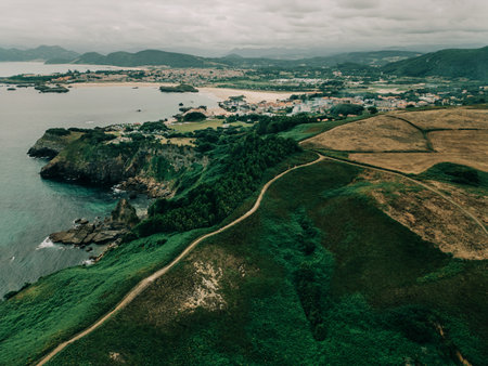 Aerial view of coastal cliffs, green hills and a seaside town under cloudy sky.の写真素材