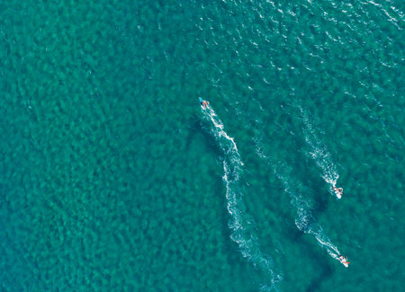 Aerial view of turquoise sea with people riding jet skis leaving white trails. Greece