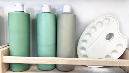 Three pastel green paint bottles and a white plastic palette stored on a wooden shelf.の写真素材