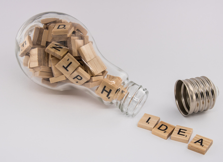 A light bulb, with an unscrewed socket, filled with letter tiles, spitting out the word "idea" on a white background.の写真素材