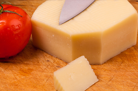 Piece of cheese, a knife and a tomato on a used wodden boardの写真素材