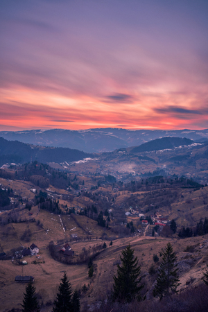 Small village placed in a valley between mountains seen from above at sunset shot in Romania with a long exposure with a mountain covered with snow in the backgroundの写真素材