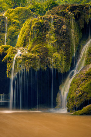 Beautiful detail of a waterfall flowing onto a moss covered rock with a cave beneath shot in Romania with a long exposureの写真素材