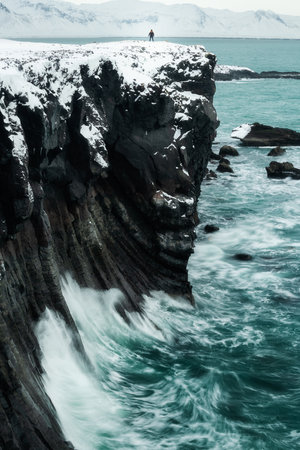 Lone hiker on top of basaltic volcano rock columns cliffs on the Atlantic Ocean shoreline, in...