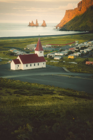 The church in the coastal town of Vik, in Southern Iceland, with the Ocean and the sea stacks in the...