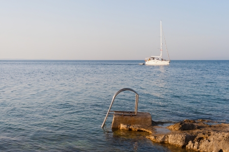 Stair for taking a bath in the rocky mediterranean sea in croatia with sailing boat in the backgroundの写真素材