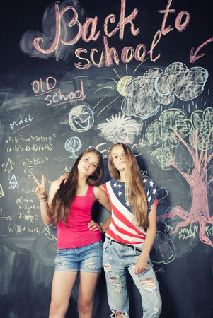 back to school after summer vacations, two teen girls in classroom with blackboard paintedの写真素材