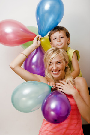 pretty family with color balloons on white background, blond woman with little boy at birthday partyの写真素材