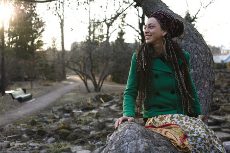 young woman sitting on tree in park smilingの写真素材
