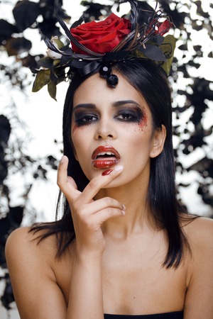 pretty brunette woman with rose jewelry, black and red, bright make up kike a vampire closeupの写真素材