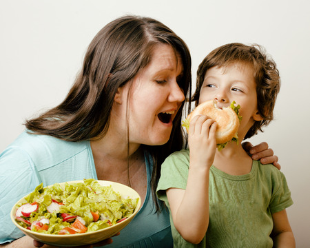 fat woman holding salad and little cute boy with hamburger teasing real familyの写真素材
