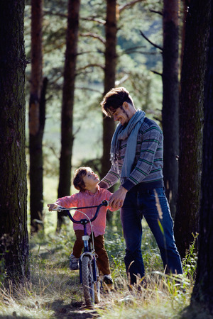 father learning his son to ride on bicycle outside in park, sunny dayの写真素材