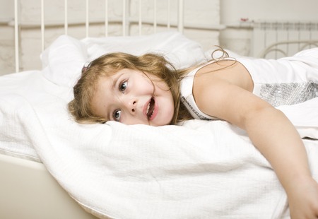portrait of little cute girl in bed at home close up, white sheetsの写真素材