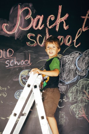 little cute real boy at blackboard in classroom, back to school