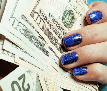 close up fingers with deep blue creative pattern manicure holding dollarsの写真素材