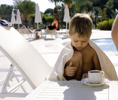 little  cute boy at swimming pool warmed up with towel and hot tea, hotel backgroundの写真素材