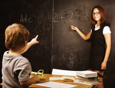 little cute real boy with teacher in classroom at desk close up, wearing glassesの写真素材