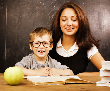 little cute real boy with teacher in classroom at desk close up, wearing glassesの写真素材