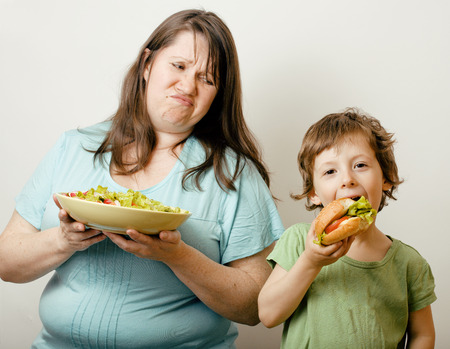 mature fat woman holding salad and little cute boy with hamburger teasingの写真素材