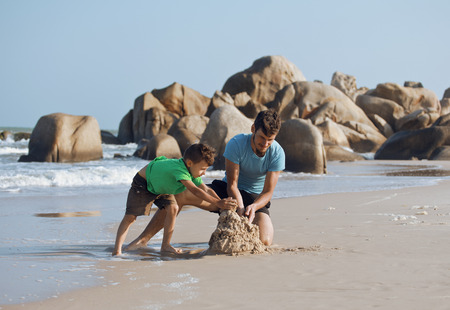 happy family on beach playing, father with son walking sea coast, rocks behind smiling taking vacationの写真素材