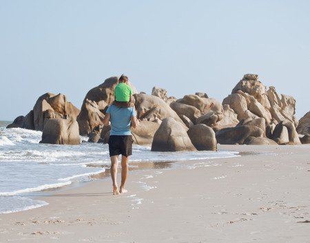 happy family on beach playing, father with son walking sea coast, rocks behind smiling taking vacationの写真素材