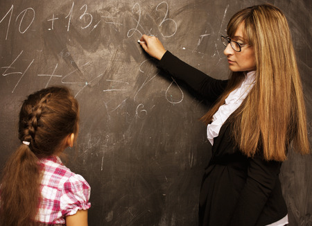teacher with pupil in classroom at blackboard writting, girl in school smilingの写真素材