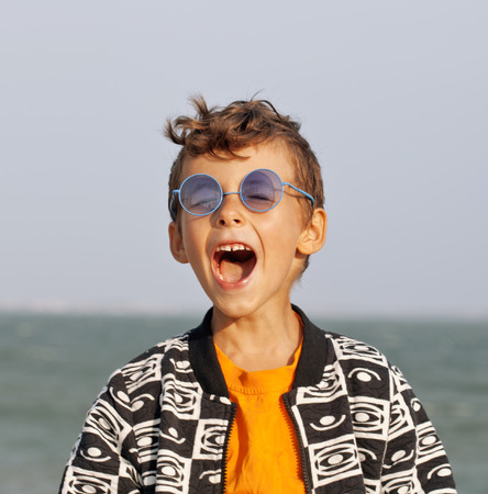 cute little boy at seacoast in fashion clothers and blue glasses close up smilingの写真素材