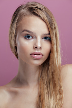 young pretty blonde real woman with hairstyle close up and makeup on pink background smilingの写真素材